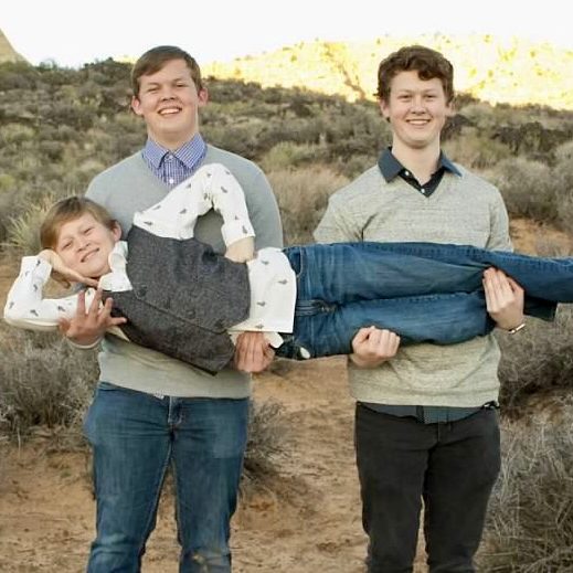 Three brothers, the two bigger brothers are holding the littlest brother across there arms forming an "H"